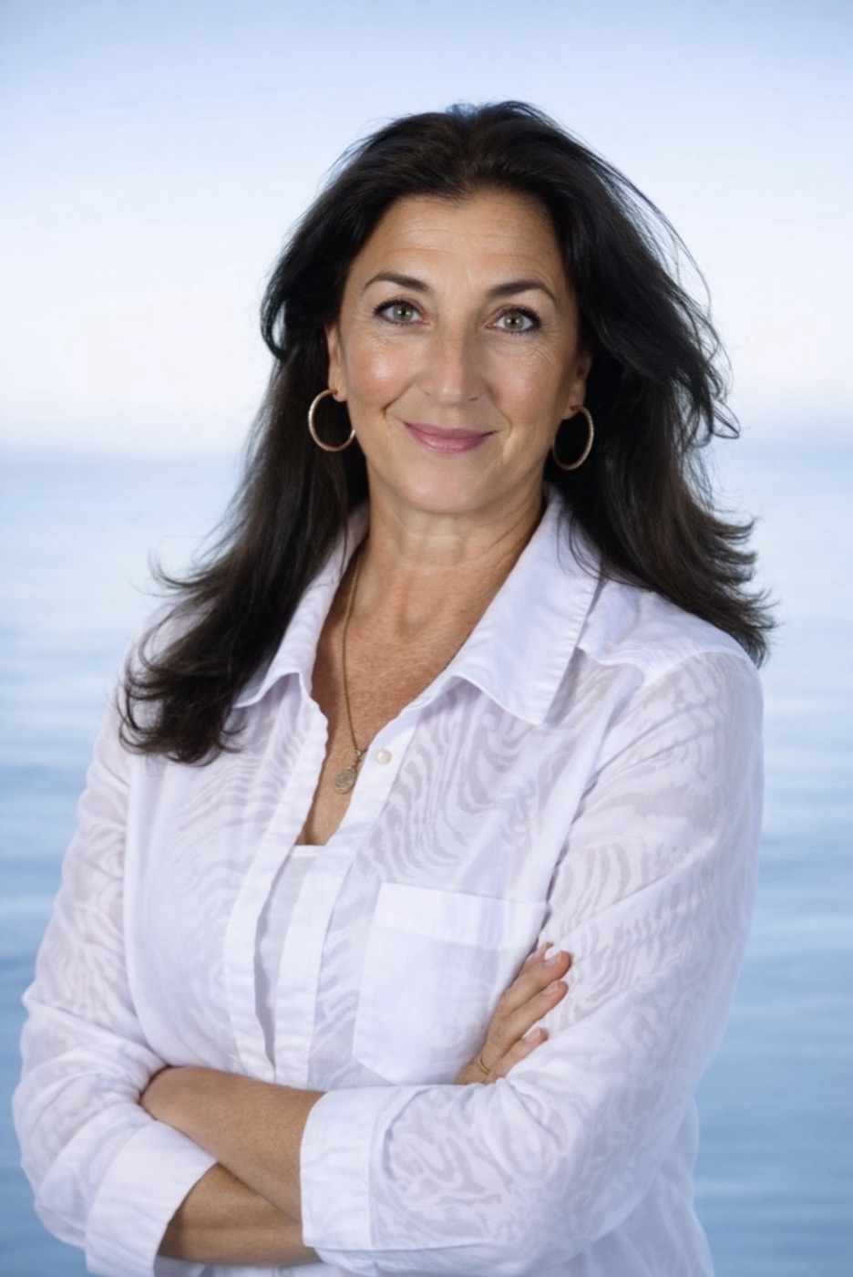 Ria Ruane smiling in a white shirt with the sea behind her